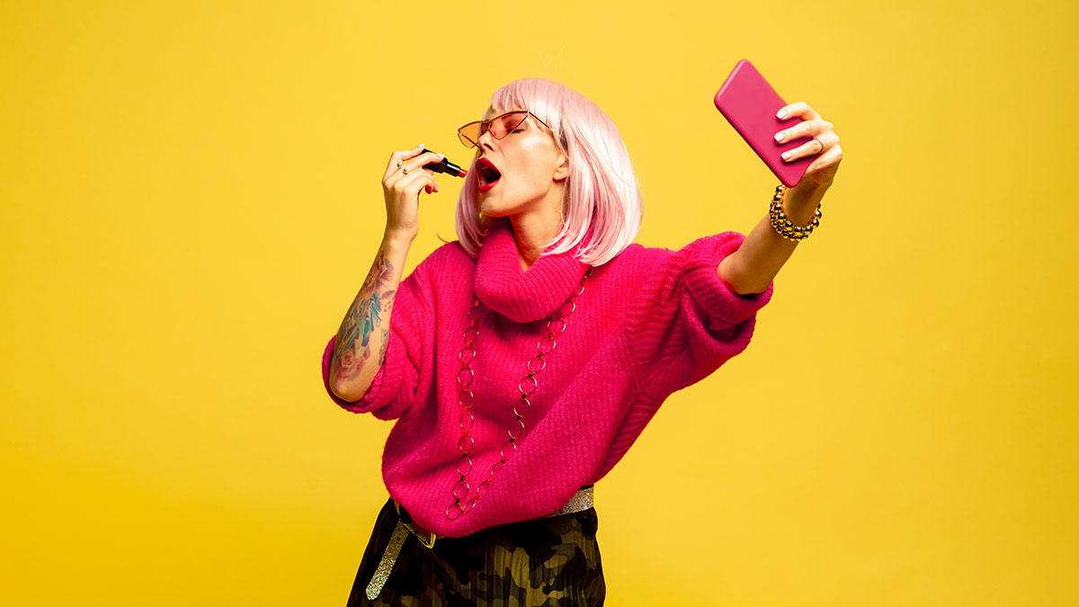 marketing de influencers Chica influencer de cabello rosa usa labial mientras se toma un selfie